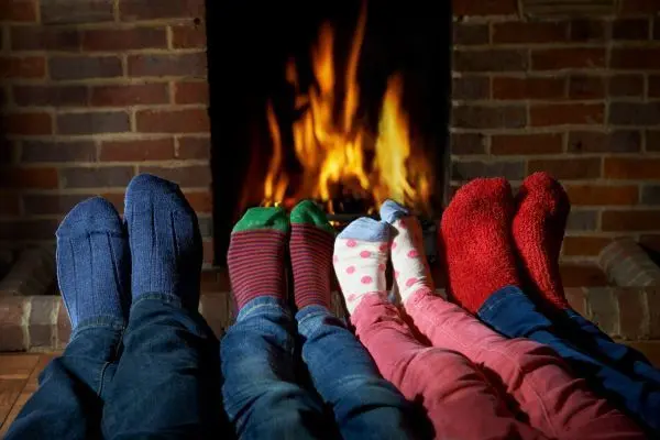 Eine Familie trägt bunte Socken und streckt die Füße in Richtung des Kaminfeuers.