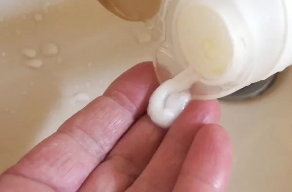 Eine Hand hält eine flüssige Spülung, die aus einer Flasche fließt, während sie über einem Waschbecken steht.