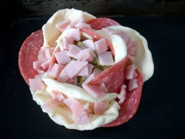 In die Rosenmitte dann auf das Pesto und auch zwischen die Blütenblätter den Schinken geben.