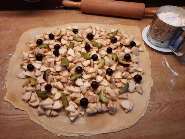 Hier sieht man den ausgerollten Strudelteig mit dem bunten Belag aus Äpfeln, Trauben und Zwetschgen.