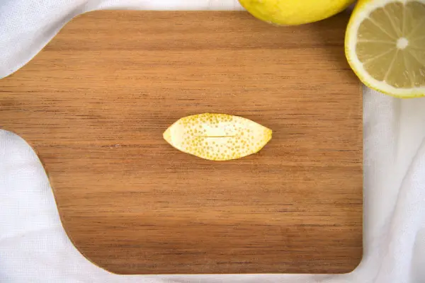 Schneide die Zitronenschale ovalförmig aus und mache mittig einen kleinen Schnitt.