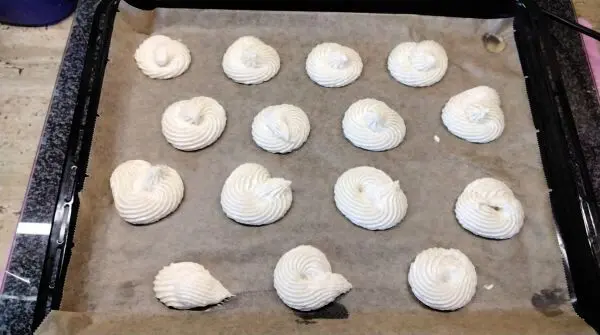 Mit einem Spritzbeutel wird der Teig auf ein mit Backpapier ausgelegtes Backblech mit etwas Abstand gespritzt.