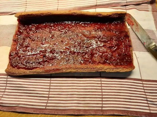 Sobald der Boden abgekühlt ist, wird die Preiselbeerfüllung gleichmäßig auf der Schokobiskuitrolle verteilt.