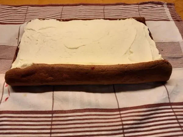 Auf die Preiselbeerfüllung wird sogleich die Quarksahnefüllung verteilt. Dann wird wieder aufgerollt.