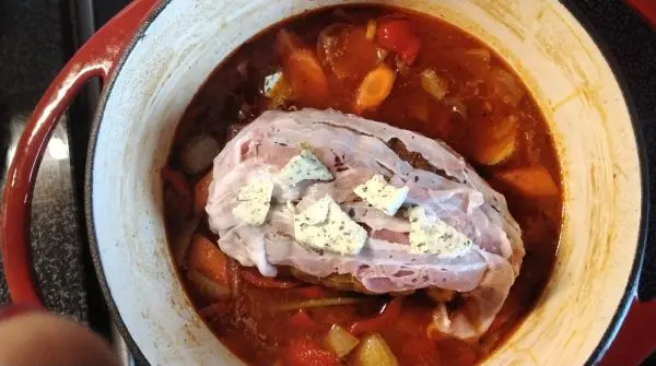 Der gewürzte Rollbraten wird in den Soßenansatz gelegt. Oben auf habe ich ein paar Gewürz-Butter-Stücke gelegt.