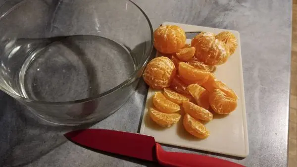 In eine große Glasschüssel werden die kernlosen geschnittenen Mandarinenstücke hineingeben. In eine große Glasschüssel werden die kernlosen geschnittenen Mandarinenstücke hineingeben.