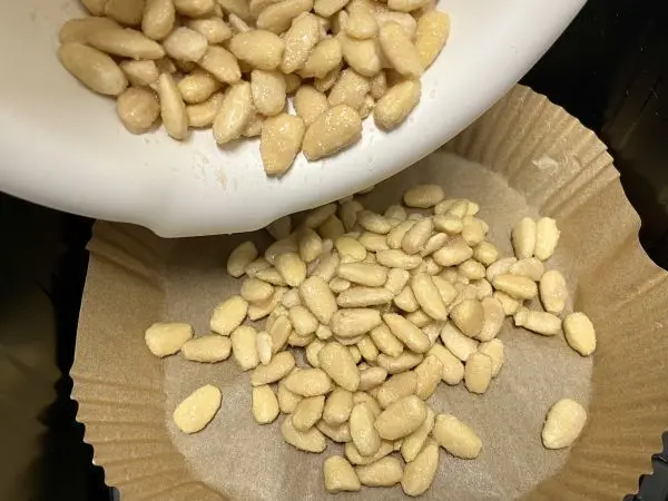 Die Mandeln auf ein Backpapier in den Airfryer füllen und gleichmäßig verteilen. Die Mandeln auf ein Backpapier in den Airfryer füllen und gleichmäßig verteilen.