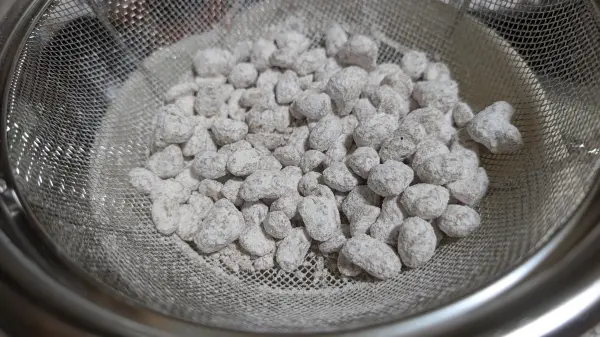 Nun die Erdnüsse in ein Sieb geben, um den überschüssigen Puderzucker loszuwerden. Nun die Erdnüsse in ein Sieb geben, um den überschüssigen Puderzucker loszuwerden.