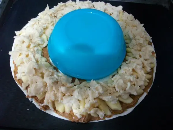 Das Crumble mit den Fingern zerbr&ouml;seln und einigerma&szlig;en gleichm&auml;&szlig;ig &uuml;ber die &Auml;pfel verteilen. Den Teigrand au&szlig;en etwas einrollen.