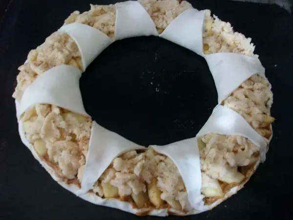 Die mittigen Teigteile zieht man dann an der Spitze &uuml;ber den Apfelring r&uuml;ber und dr&uuml;ckt sie am Rand fest.