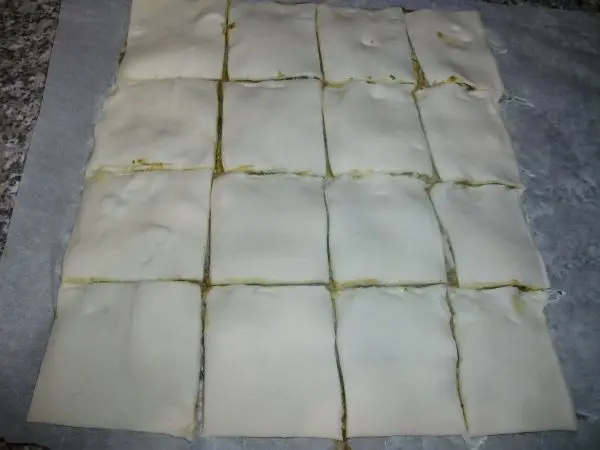 Die zweite Hälfte Blätterteig darauf legen und leicht andrücken. Vorsichtig in etwa gleich große Quadrate schneiden. Die zweite Hälfte Blätterteig darauf legen und leicht andrücken. Vorsichtig in etwa gleich große Quadrate schneiden.