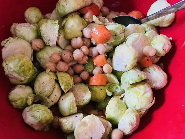 Rosenkohl, Kichererbsen und M&ouml;hren werden mit &Ouml;l, Salz und Pfeffer in einer Sch&uuml;ssel anger&uuml;hrt.