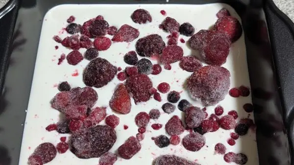 Die H&auml;lfte des Joghurts in eine quadratische Form geben und obendrauf die gefrorenen Beerenfr&uuml;chte.