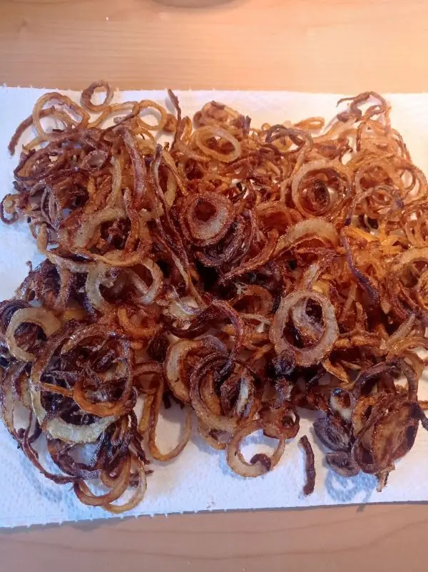 Die frittierten Zwiebeln k&ouml;nnen auf einem K&uuml;chenkrepp entfetten und werden dann zur Seite gestellt.