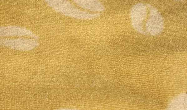 Ein gelber Teppich mit einem Muster aus Kaffeesatzbechern liegt entspannt auf dem Boden in einem hellen Raum.
