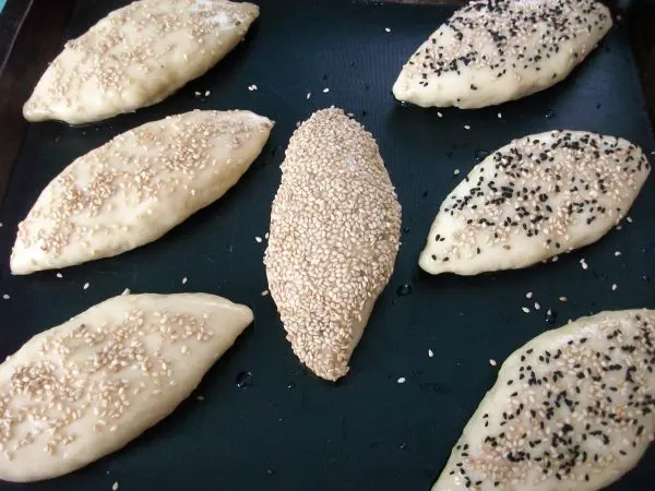 Pogaca Naht nach unten aufs Blech legen und die mit Sirup bepinselte Oberseite mit etwas Sesam bestreuen. Oberseite einschneiden.