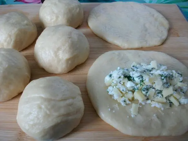 Den Teig in ca. 7 gleich gro&szlig;e St&uuml;cke teilen, zu Kugeln formen, diese platt dr&uuml;cken und die K&auml;sef&uuml;llung in die Mitte geben.