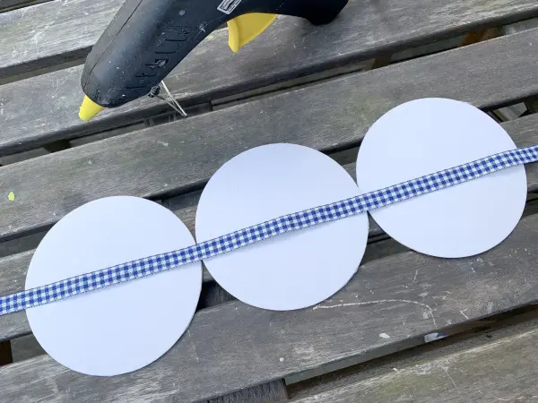 Die Bierdeckel werden in einer Reihe angeordnet und mithilfe von Stoffband und Hei&szlig;kleber fixiert.