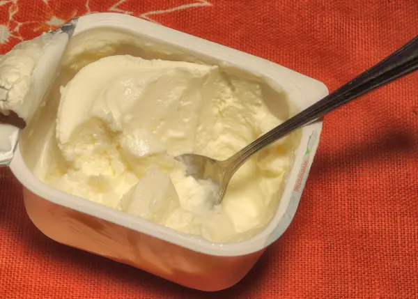 Eine Schale Quark steht auf einem roten Tuch, während ein Löffel dabei ist, um den Quark zu servieren.