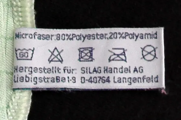 Ein Pflegeetikett zeigt die Zusammensetzung von Mikrofaser-Bettbezügen, die weniger Staub enthalten.