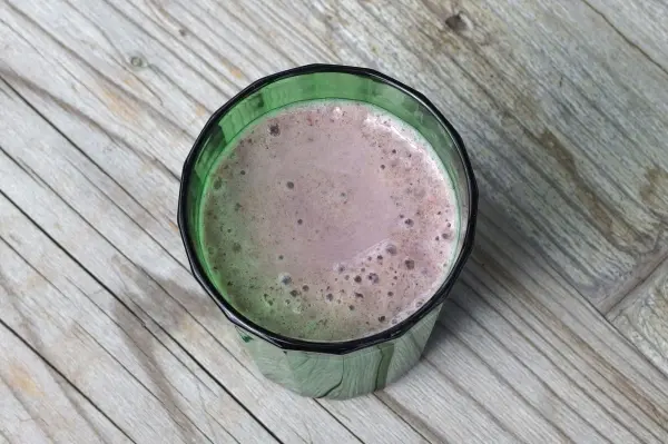 Ein grüner Becher mit einem schaumigen Getränk auf einer rustikalen Holzoberfläche. Abkühler zum Trinken.