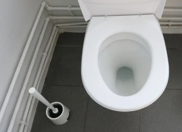 Ein weißesWC mit einer Toilettenbürste daneben, in einem modernen Badezimmer. Ränder können hier mit Scheuerpulver behandelt werden.