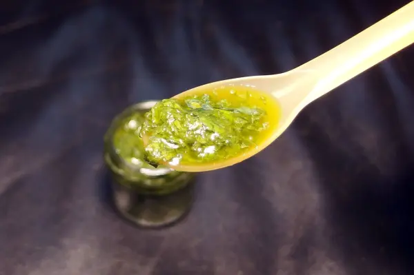 Eine Löffel mit grünem Pesto steht über einem kleinen Glas, während der Hintergrund dunkel gehalten ist, um das Pesto hervorzuheben.