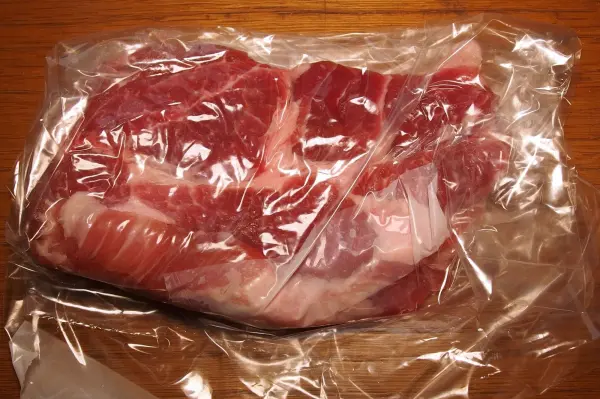 Ein rohes Schnitzel liegt in Plastikfolie auf einem Holztisch, bereit zum Klopfen ohne Spritzen.