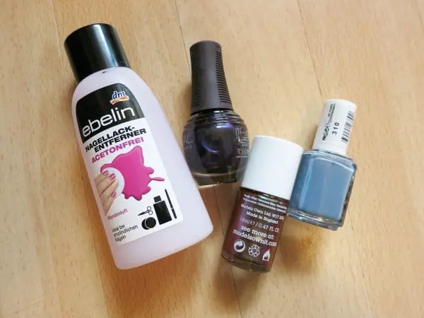Ein Fläschchen Nagellackentferner steht neben mehreren Nagellacken auf einem Holztisch, bereit zum Verflüssigen.