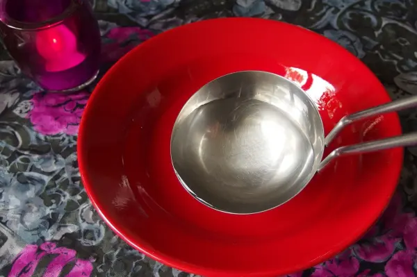 Eine rote Schale steht auf einem bunten Tisch mit einer silbernen Kelle daneben, bereit für eine ostfriesische Tomatensuppe.