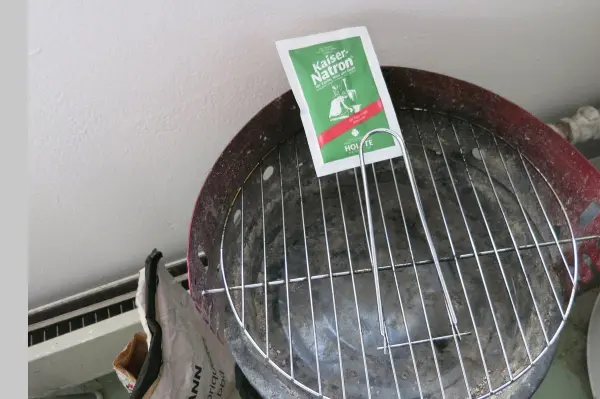 Ein Grillrost liegt auf einem Holzkohlegrill, während eine Packung Natron daneben steht, bereit zur Reinigung.