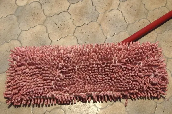 Ein roter Wischmopp liegt auf einem fliesenartigen Boden, bereit zum Waschen, um für die Reinigung verwendet zu werden.
