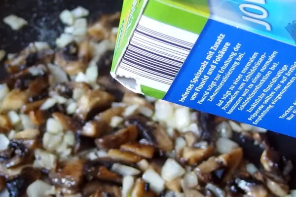 In einer Pfanne braten knackige, crosse Pilze mit Zwiebeln, während eine Flüssigkeit aus einem Karton darüber gegossen wird.