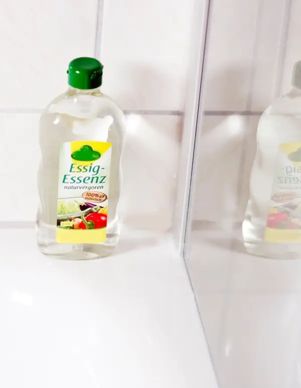 Eine Flasche Essig-Essenz steht auf einem weißen Waschbecken in einem Badezimmer und reflektiert im Spiegel.