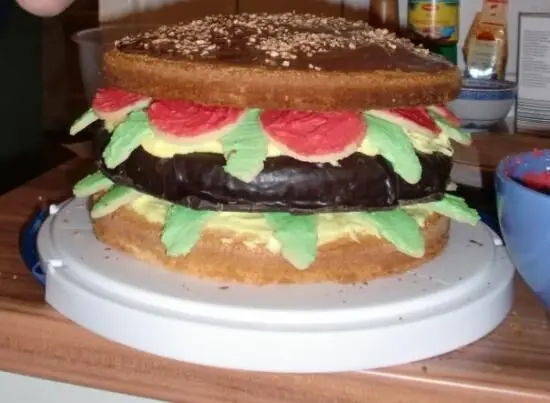Eine Torte im Stil eines Big Macs mit bunten Schichten aus Fondant und Schokolade steht auf einem Tisch in der Küche.