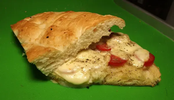 Ein Döner mit Tomate und Mozzarella liegt auf einem grünen Brett, aufgeschnitten und bereit zum Genuss.