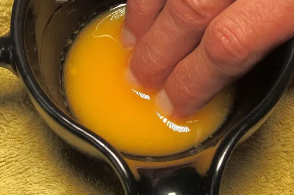 Eine Hand mit gepflegten Fingernägeln taucht in eine Schüssel mit frischem Ei, um die Nägel zu stärken und zu pflegen.