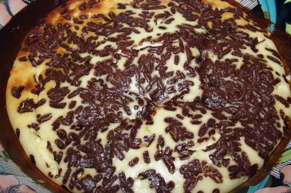 Ein cremiger Ofenquark mit Schokoladenstückchen ist goldbraun gebacken und auf einem Teller angerichtet, umgeben von buntem Geschirr.