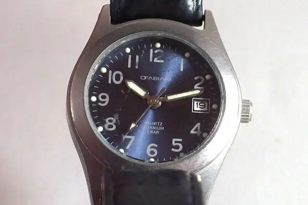 Eine Uhr mit Plexiglasglas liegt auf einer hellen Oberfläche, Kratzer sind sichtbar, was die Oberfläche beeinträchtigt.
