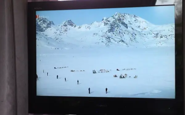 Ein Fernseher zeigt eine schneebedeckte Landschaft mit Menschen, die sich im Winter am Berg bewegen.