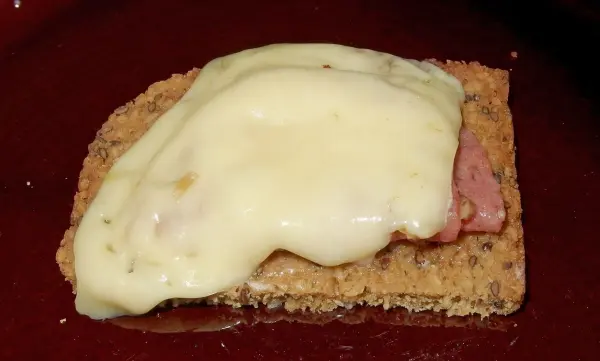 Eine Scheibe Brot liegt auf einem Teller, belegt mit Schinken und geschmolzenem Käse, ideal für ein leckeres Snack.