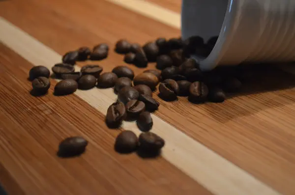 Kaffeebohnen fallen aus einer Tasse auf ein Holzbrett, ideal für die Zubereitung von gutem italienischen Kaffee.