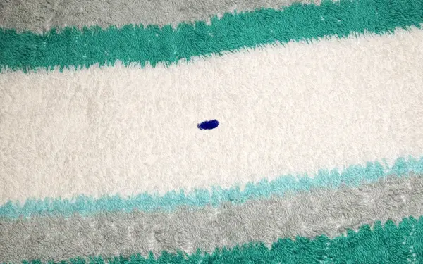 Auf einem gestreiften Handtuch liegt ein kleiner blauer Kugelschreiberfleck, der die Oberfläche verschmutzt.