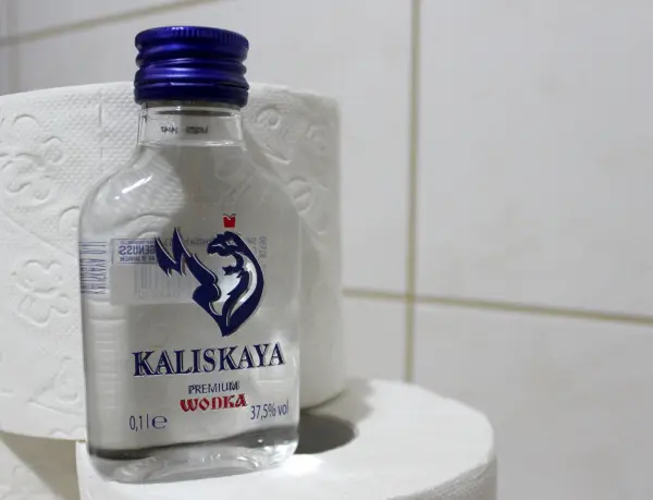 Eine Flasche Wodka steht auf einem Toilettenpapierstapel in einem Badezimmer, was auf einen möglichen Durchfall hinweist.