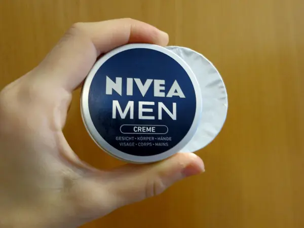 Eine Hand hält eine runde Dose mit Nivea Men Creme, die zur Hautpflege verwendet wird, vor einer Holzoberfläche.