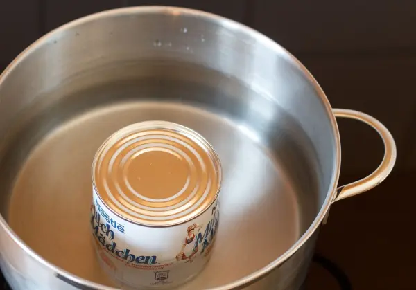 Eine Dose mit Milchcondensat schwimmt in einem Topf mit Wasser, um Dulce de leche durch Erhitzen zu erzeugen.
