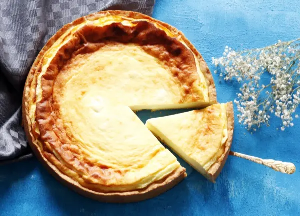 Ein Käsekuchen liegt auf einem blauen Untergrund, mit einem Stück herausgeschnitten und einer Gabel daneben.