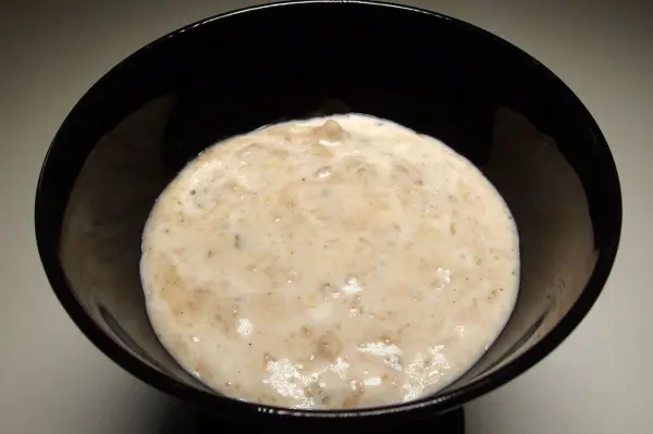 Eine cremige, beige Dessertmasse aus Spekulatiusresten liegt in einer schwarzen Schüssel auf einem neutralen Hintergrund.