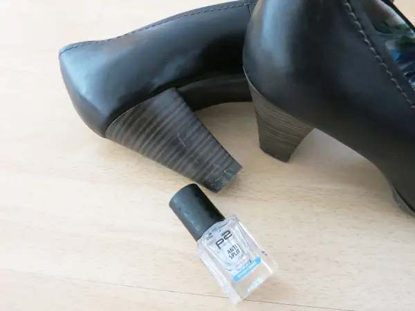 Schwarze Schuhabsätze stehen neben einer Flasche Klarlack auf einem hellen Tisch, bereit für die Pflege und den Schutz.