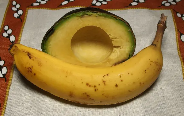Eine auf einem Tuch liegende Banane neben einer halbierten Avocado, bereit für eine cremige Zubereitung.